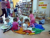 Dzieci siedzą na chuście i oglądają książeczki z naszych zbiorów.