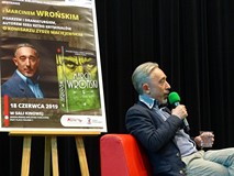 Marcin Wroński podczas spotkania. Po jegolewej stronie widoczny plakat promujący to spotkanie.