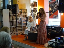 Od lewej: Alicja Flis, Jola Tubielewicz podczas występu. Alicja Flis siedzi, Jola Tubielewicz śpiewa