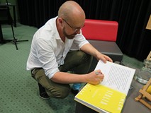 Bartek Kieżun kuca przy stoliku, składa pamiątkowy autograf w książce swojego autorstwa