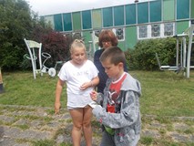 Dzieci wykonują zadania na dworze w grupach pod czujnych okiem Pani Grażyny