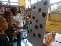 Prowadząca warsztaty stoi przed tablicą i pokazuje dzieciom zapisane pomysły na dbanie o środowisko