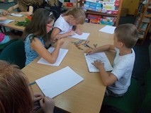 Dzieci siedzą przy stolikach podczas wykonywania pracy plastycznej