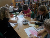 Dzieci siedzą przy stolikach podczas wykonywania pracy plastycznej