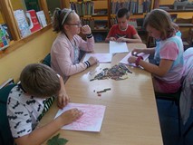 Dzieci siedzą przy stolikach podczas wykonywania pracy plastycznej