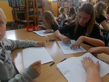 Dzieci siedzą przy stolikach podczas wykonywania pracy plastycznej