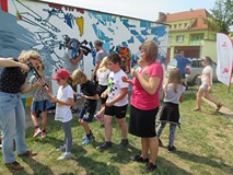 Dzieci uczestniczące w akcji tworzenia muralu podczas nakładania kleju na plastikowe nakrętki