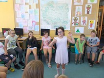 Dzieci siedzą na krzesłach, a dziewczynka stoi w środku i opowiada bajkę