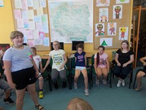 Dzieci siedzą na krzesłach, a dziewczynka stoi w środku i opowiada bajkę