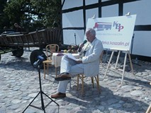 Aktor Piotr Krótki siedzi przy stoliku i czyta podczas Narodowego Czytania 2019