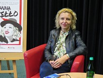 Joanna Jagiełło siedzi po spotkaniu na czerwonym fotelu. Po lewej stronie widać fragment plakatu pro