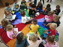 Dzieci siedzą na chuście i oglądają książeczki z naszych zbiorów.