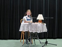 Uczestniczka konkursu Wybieramy Mistrza Pięknego Czytania siedzi przy stoliku i czyta. Na stoliku je