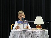 Uczestnik konkursu Wybieramy Mistrza Pięknego Czytania siedzi przy stoliku i czyta. Na stoliku jest 