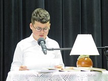 Uczestnik konkursu Wybieramy Mistrza Pięknego Czytania siedzi przy stoliku i czyta. Na stoliku jest 