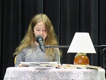 Uczestniczka konkursu Wybieramy Mistrza Pięknego Czytania siedzi przy stoliku i czyta. Na stoliku je