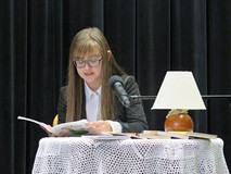 Uczestniczka konkursu Wybieramy Mistrza Pięknego Czytania siedzi przy stoliku i czyta. Na stoliku je