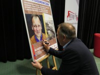 Cezary Łazarewicz składa pamiątkowy autograf na plakacie promującym spotkanie w KBP