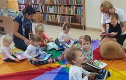 Dzieci siedzą na chuście i oglądają książeczki z naszych zbiorów.