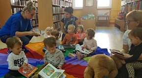 Dzieci siedzą na chuście i oglądają książeczki z naszych zbiorów.