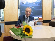 Eugeniusz Żuber siedzi przy okrągłym stoliku przy otwartej swojej książce. Na stoliku leży słoneczni