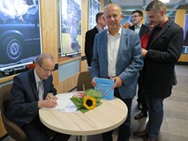 Eugeniusz Żuber składa pamiątkowe podpisy. Wokół niego stoją czytelnicy. Jan Kuriata prezentuje najn