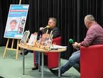 Od lewej: Plakat promujący spotkanie, Robert Makłowicz, Piotr Pawłowski. Przed nimi stolik z książka
