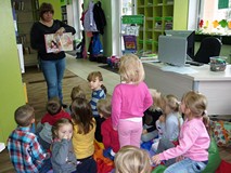 Dzieci siedzą na podłodze i słuchają bibliotekarki