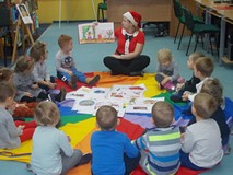 Dzieci siedzą na chuście i słuchają opowiadania czytanego przez bibliotekarkę przebraną za panią mik