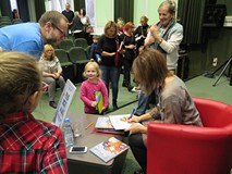 Agata Widzowska w otoczeniu dzieci. Autorka robi pamiątkowe wpisy.