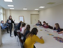 Uczestnicy warsztatów z Sarą Olszewską siedzą przy stole i rysują renifera. Widać prowadzącą warszta