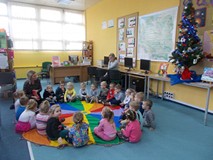 Dzieci siedzą na chuście animacyjnej i słuchają czytnego przez bibliotekarkę opowiadania