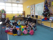 Dzieci siedzą na chuście animacyjnej i słuchają czytnego przez bibliotekarkę opowiadania