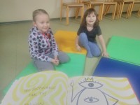 Dwie dziewczynki podczas zajęć siedzą na materacach i słychają czytanej książki