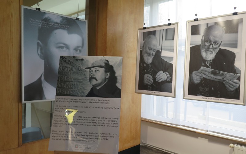 Tablica rozpoczynająca wystawę ze zdjęciem i biogramem Zygmunta Wujka, w tle widać trzy...