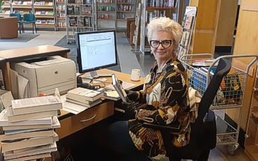 Bibliotekarze nadrabiają zaległości. Bibliotekarka przy biurku pełnym książek.