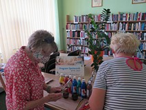 Na tle regałów z książkami uczestniczki warsztatów Maria Szlachcikowska i Teresa Dąbrowska wybierają