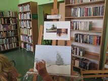 Na tle regałów z książkami na sztaludze stoi szkic obrazu Danuty Nadolskiej. Widać również bok twarz