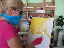 Na tle regałów z prasą Elżbieta Knitter rozpoczyna malowanie obrazu.