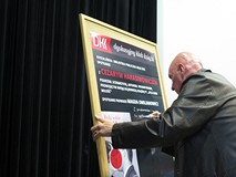 Cezary Harasimowicz składa pamiątkowy podpis na plakacie promującym spotkanie
