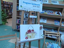 na zdjęciu obraz Wandy Kołtun - czerwone jabłka, w brązowym koszyku. U góry plakat Program Społeczni