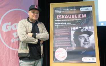 Bartłomiej Skubisz stoi na scenie obok plakatu promującego wydarzenie