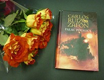 na zdjęciu na czarnym tle kwiaty oraz książka Carlosa Ruiz Zafona Pałac Północy