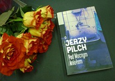 na zdjęciu na czarnym tle kwiaty oraz książka Jerzego Pilcha Pod mocnym aniołem