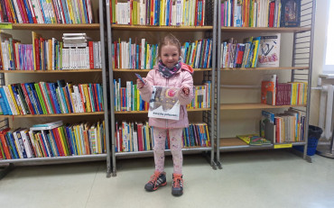 Dziewczynka trzyma w rękach książkę oraz kartę z akcji Mała Książka - Wielki...