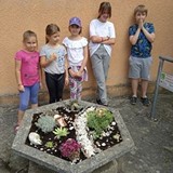 Dzieci stoją wokół gazonu, który samodzielnie obsadzili i udekorowali.