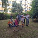 Dzieci siedząc na huśtawkach słuchają pogadanki przyrodniczej