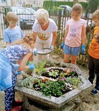Prowadząca zajęcia i dzieci stoją wokół gazonu, który samodzielnie obsadzili i udekorowali.