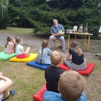 Spotkanie autorskie w ogrodzie Filii nr 9 KBP. Pawł Wakuła, autor książek dla dzieci rozmawia z uczestnikami Bezpiecznych Wakacji.