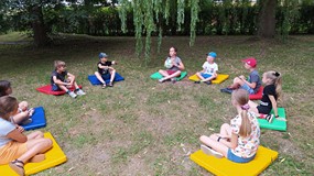 Dzieci siedzące na materacach w ogrodzie w trakcie zabawy integracyjnej